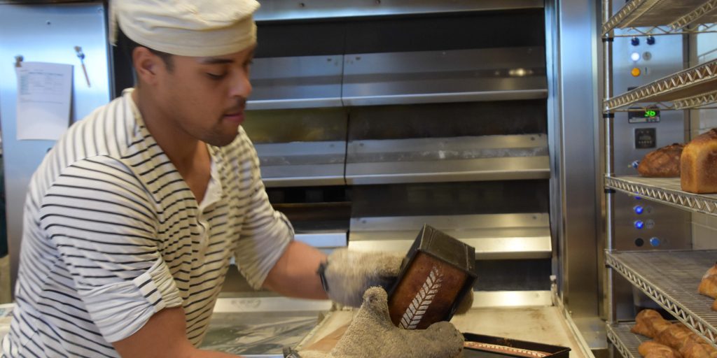 Peter in baker’s cap and gloves handles a pave. The oven is in the background.